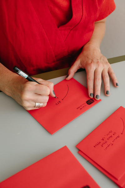 Michelle hand addresses each subscribers mailing envelope to mail the postcard of the month